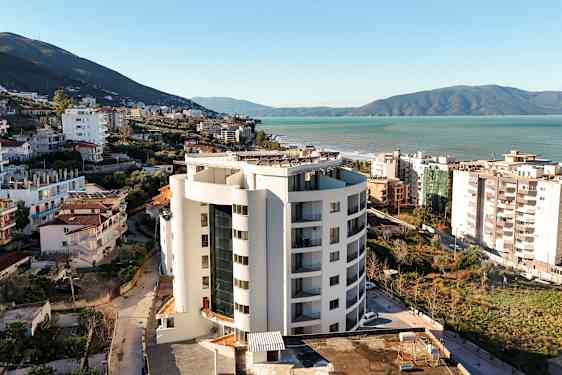 Ett höghus nära havet med omgivande byggnader och grönska. (AI-genererad text)