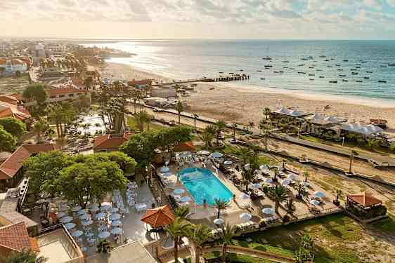 Flygfoto av en strand med solstolar och parasoller nära en pool, omgiven av grönska. (AI-genererad text)