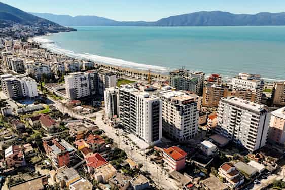 Bilden visar en stad med höghus och bostäder nära en kustlinje med sandstrand och palmer. (AI-genererad text)