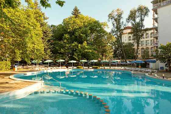 En utomhuspool med omgivande grönska och solstolar. (AI-genererad text)