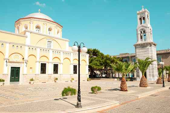 En gul byggnad med kupol och en klocktorn samt palmer och gatlykta. (AI-genererad text)