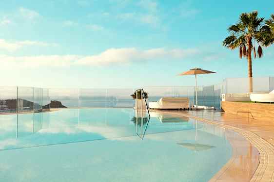 En infinitypool med utsikt över havet, omgiven av solsängar och palmer. (AI-genererad text)