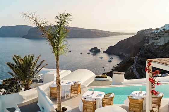 Uteservering med utsikt över havet och en klippig kustlinje, omgiven av vit arkitektur och växter. (AI-genererad text)