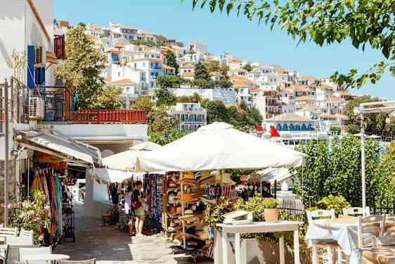 En pittoresk stadsbild med vita hus med röda tak på en sluttning, parasoll och försäljningsstånd i förgrunden. (AI-genererad text)