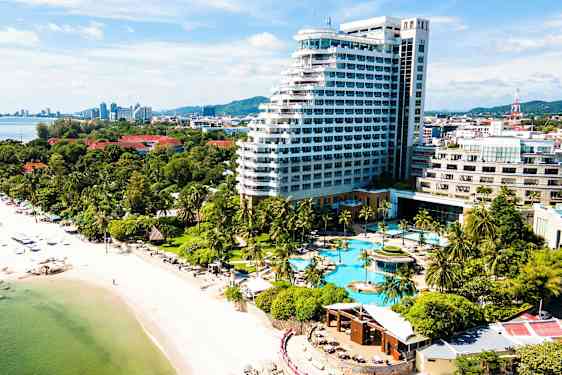 Bild av en kust med en sandstrand, palmer och ett stort hotellkomplex med poolområde. (AI-genererad text)