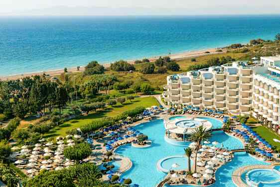 En vy över en resort med poolområden, solstolar, grönområden och havet i bakgrunden. (AI-genererad text)