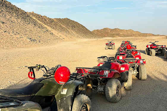 En rad fyrhjulingar står parkerade på en ökenväg, omgivna av sandiga kullar. (AI-genererad text)