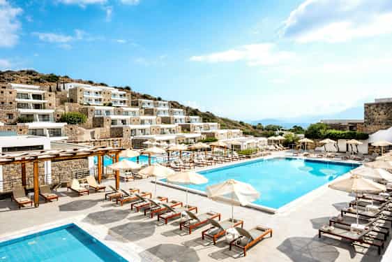 Bild av hotell med flera byggnader, pool och solstolar utomhus. (AI-genererad text)