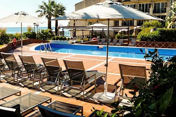 En utomhuspool med solstolar och parasoller. (AI-genererad text)