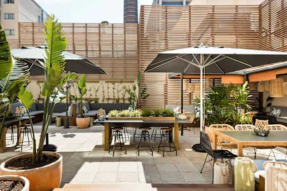 En utomhus terrass med bord, stolar och växtdekorationer, omgiven av träpaneler. (AI-genererad text)