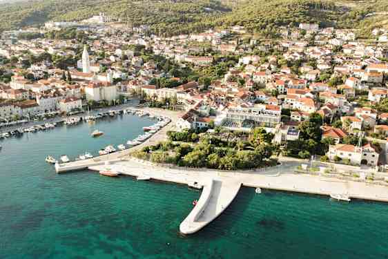 Flygfoto av en kuststad med båtar i en hamn och hus med röda tak. (AI-genererad text)