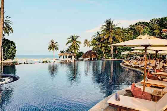 En infinitypool omgiven av solstolar och parasoller med utsikt över den tropiska miljön och havet. (AI-genererad text)