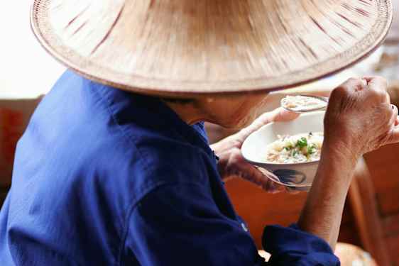 En person i blå klädsel och en hatt äter från en skål med sked. (AI-genererad text)