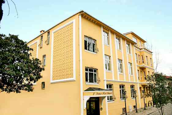 Ett gult hotell med dekorativ fasad, fönster med järngaller och en ingång med takskydd. (AI-genererad text)