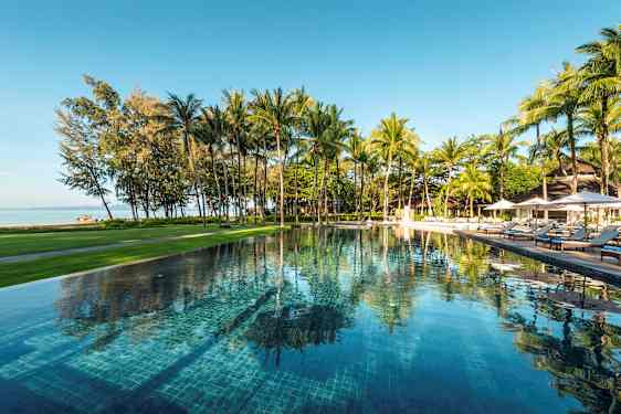 En utomhuspool omgiven av grönska och palmer, med utsikt över stranden och havet. (AI-genererad text)