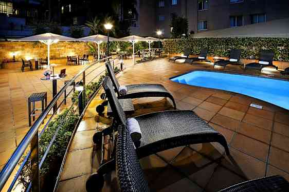 Hotellets poolområde med solstolar och parasoll vid ett upplyst och kaklat uteområde. (AI-genererad text)