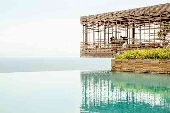 En utsikt över en infinitypool med havet i bakgrunden och en träpaviljong som svävar vid kanten. (AI-genererad text)