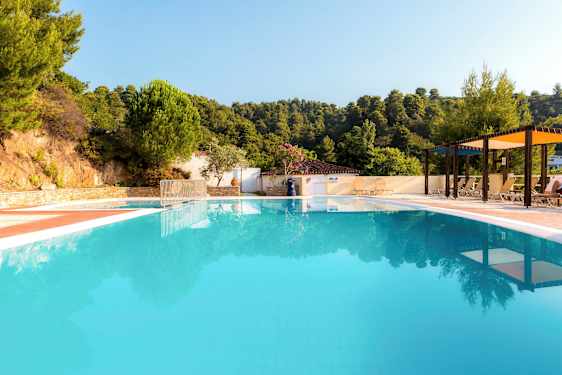 Utomhuspool omgiven av solstolar och parasoll med grönskande bakgrund. (AI-genererad text)