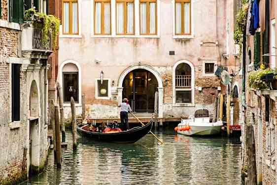 En gondol med en gondoljär flyter på en kanal framför en byggnad. (AI-genererad text)