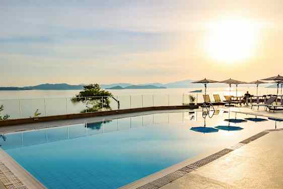 En swimmingpool med utsikt över havet och solnedgången, parasoller och solstolar vid kanten. (AI-genererad text)