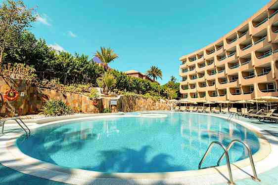 Bild av en pool med omgivande solstolar och ett flervåningshotell i bakgrunden. (AI-genererad text)