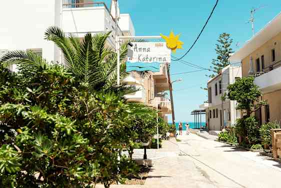 En solig gata med grönska, byggnader och en skylt som visar 'Anna Katerina'. (AI-genererad text)