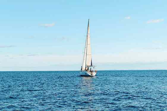 En segelbåt seglar på ett öppet hav under en klar himmel. (AI-genererad text)
