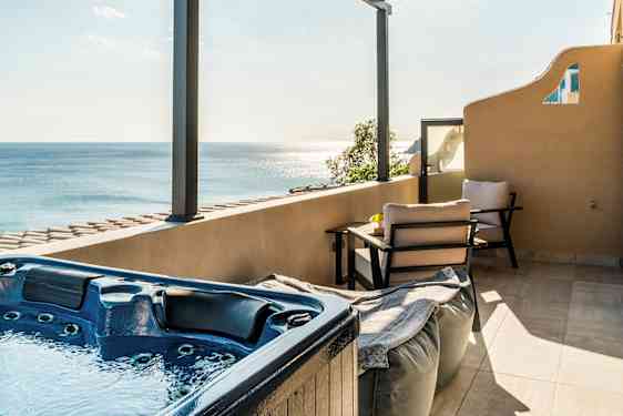 En terrass med en jacuzzi, sittmöbler och utsikt över havet under en takpergola. (AI-genererad text)