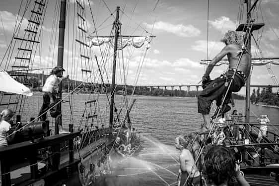 En scen på en gammaldags piratskepp med människor som interagerar och vattenspridning mellan båtar. (AI-genererad text)
