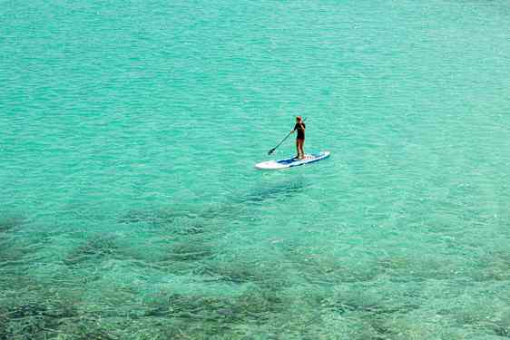 Person som paddlar stående på en paddleboard i klart turkost vatten. (AI-genererad text)