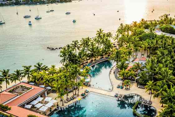 En strandresort med en pool omgiven av palmer och solstolar nära havet. (AI-genererad text)