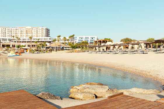 Strand med solstolar och parasoller, hotellbyggnader i bakgrunden. (AI-genererad text)