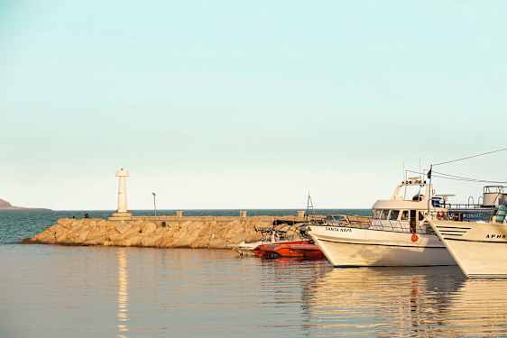 En hamn med båtar förtöjda, en fyr på en stenbrygga och lugnt vatten. (AI-genererad text)