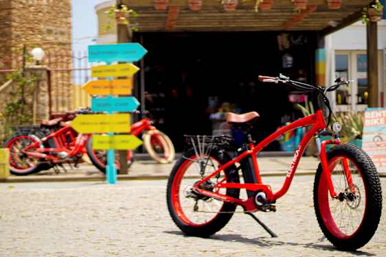 Röd cykel på kullerstensyta med färgglada vägskyltar i bakgrunden. (AI-genererad text)