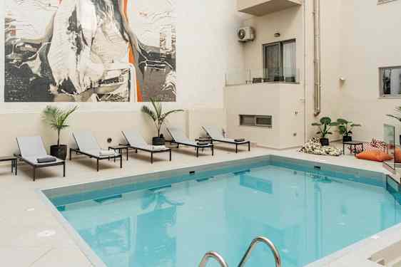 Bild av en utomhuspool vid ett hotell med solstolar och ett stort konstverk på väggen. (AI-genererad text)