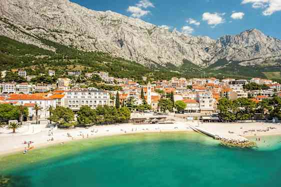 En kuststad vid foten av ett berg med en sandstrand och klart turkost vatten. (AI-genererad text)