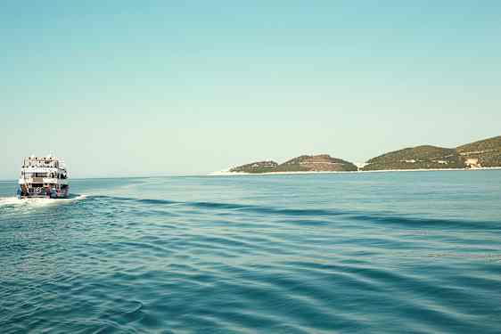 En båt färdas över ett stilla hav med några låga öar i horisonten. (AI-genererad text)