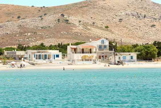 Bild av en klarblå havsvik med en sandstrand som har hus och kullar i bakgrunden. (AI-genererad text)