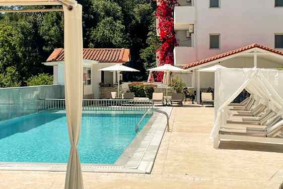 En utomhuspool med solstolar och ett vitkalkat hus i bakgrunden. (AI-genererad text)