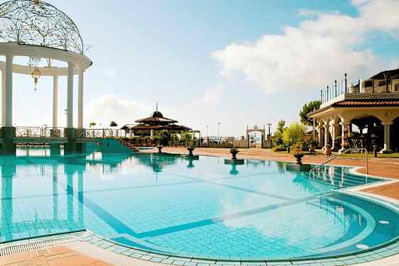 En utomhuspool med en dekorerad paviljong och omgivning av byggnader i medelhavsstil. (AI-genererad text)