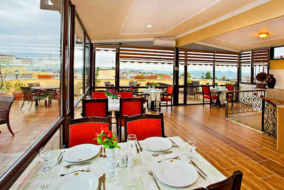 En restaurang med bord dukade för måltid, röda stolar och utsikt över en terrass samt havet. (AI-genererad text)