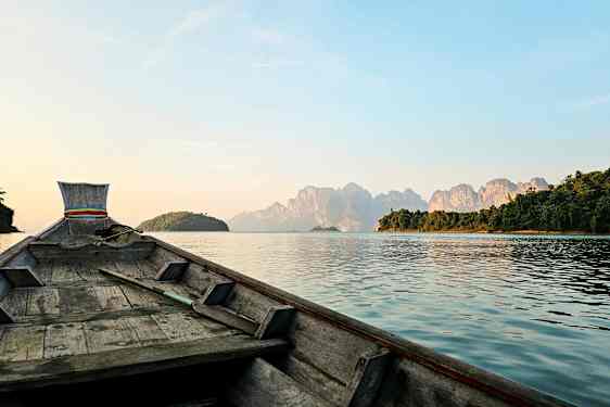 Bild av en träbåt som seglar mot berg på en sjö. (AI-genererad text)