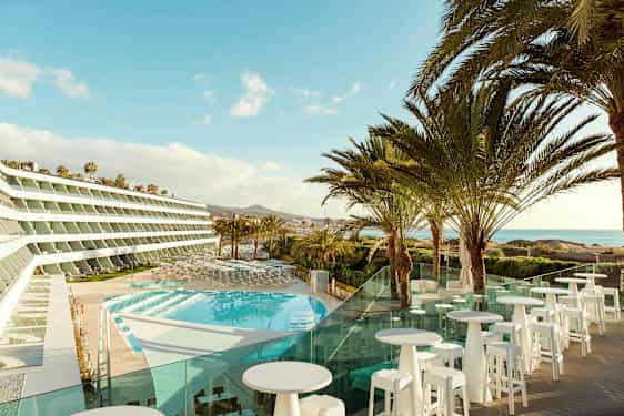 Bild av ett hotell med utsikt över en pool och palmer, med havet i bakgrunden. (AI-genererad text)