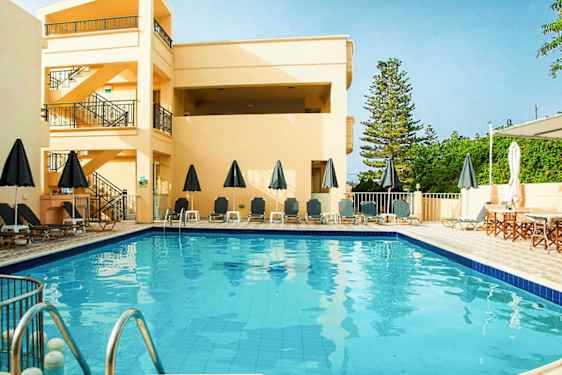 Utomhuspool med solstolar och parasoller, omgiven av byggnader och grönska. (AI-genererad text)