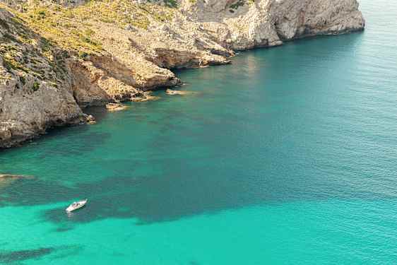 En båt ligger förankrad i klart turkost vatten nära en stenig kustlinje med klippor. (AI-genererad text)