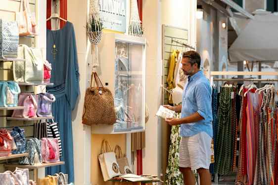 En butik vid en gata som säljer kläder och accessoarer, med väskor och klänningar synliga i skyltfönstret. (AI-genererad text)