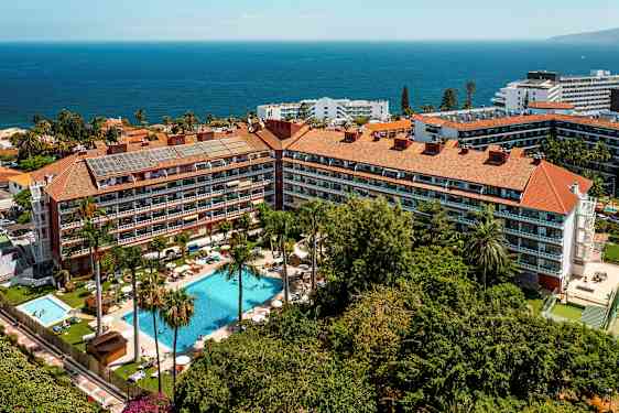 Flygfoto av ett hotellkomplex med pooler, palmer och havet i bakgrunden. (AI-genererad text)