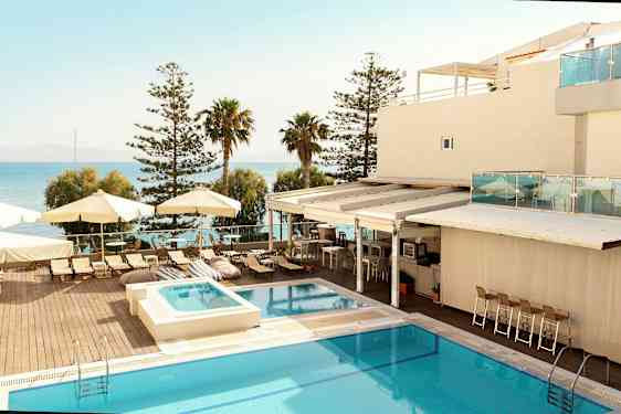 Ett hotellområde med en pool, solstolar och parasoller vid havet. (AI-genererad text)