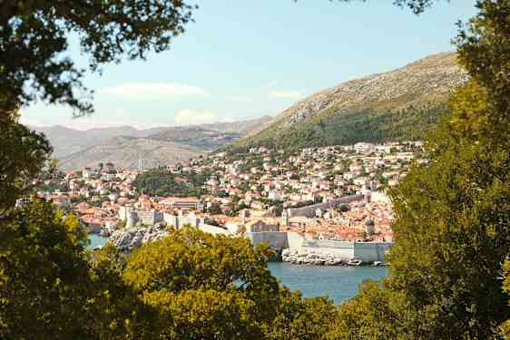 En vy över Dubrovnik med sin historiska stadsmur, omgiven av grönska. (AI-genererad text)