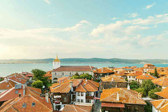 Gamla stadens tak med hus med röda tegeltak och en kyrka i bakgrunden nära havet vid kusten. (AI-genererad text)
